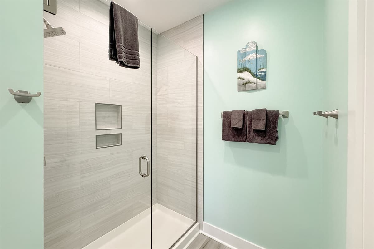 Enjoy the clean and contemporary design of this bathroom's large walk-in shower, complete with sleek light-colored tiled walls and convenient built-in niches for your toiletries. The clear glass door and light blue walls contribute to a bright and airy, sp