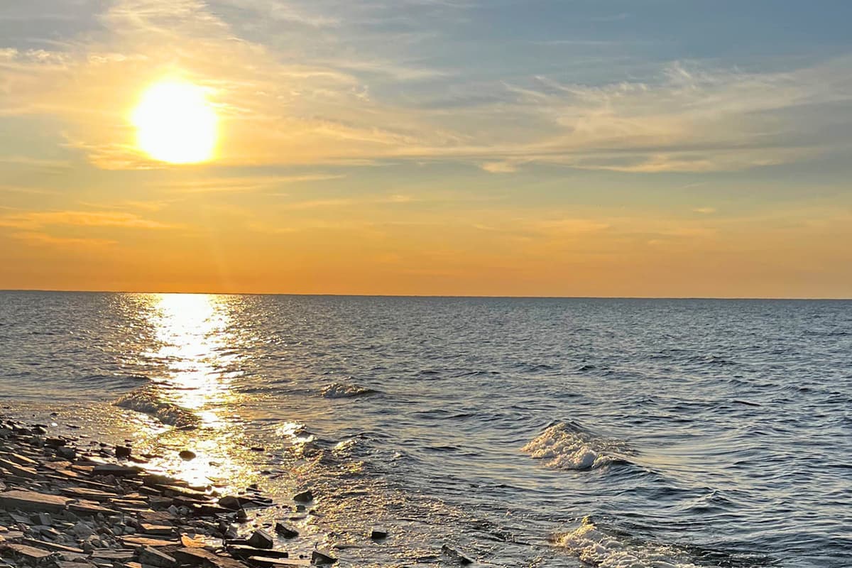 The calm shoreline creates a peaceful setting as the sky fills with warm sunset colors. It’s a lovely spot to relax, take photos, or simply enjoy a quiet moment by the water. As the sun dips