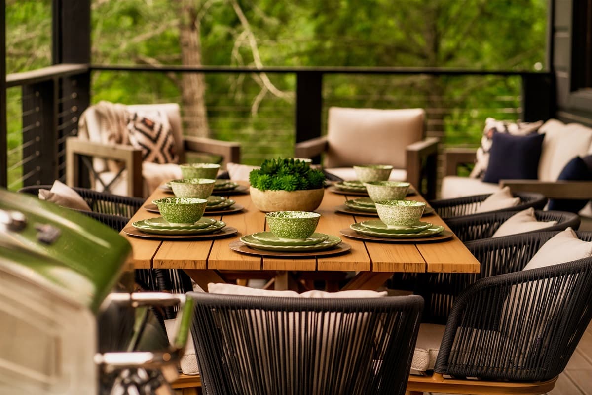 The outdoor dining table is beautifully set with green dishware and a charming centerpiece, ready for an al fresco meal amidst nature.