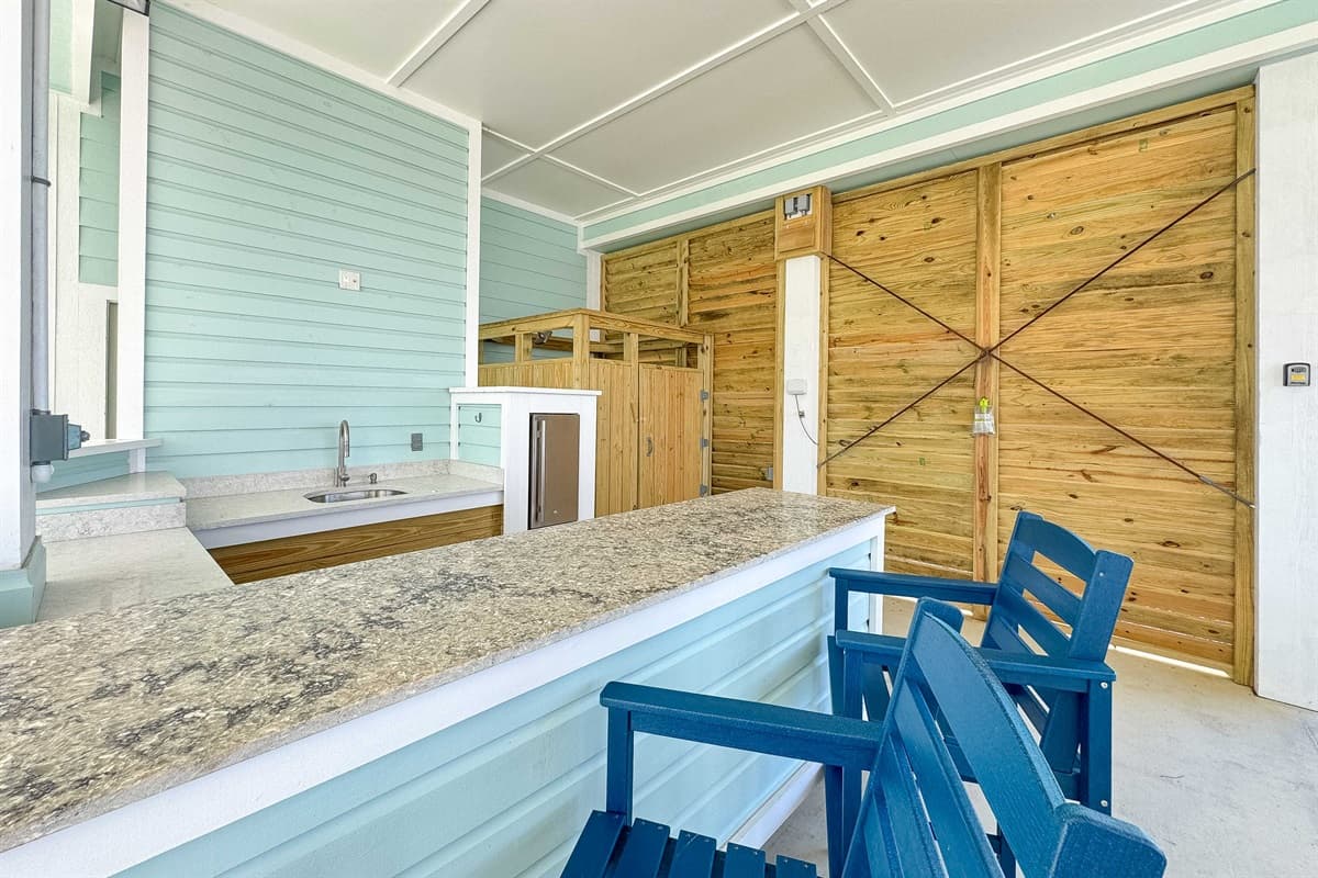 Perfect for outdoor gatherings, this dedicated area boasts a convenient wet bar with ample counter space and a sink, along with several bar stools for guests to relax. The appealing blue-green shiplap walls and rustic wooden elements, including private out