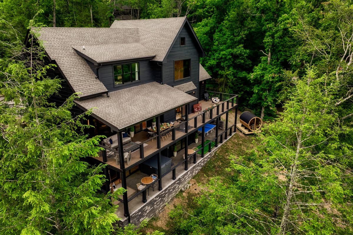 This impressive modern mountain retreat features multiple levels of expansive decks, surrounded by lush forest, and even includes a unique barrel sauna.
