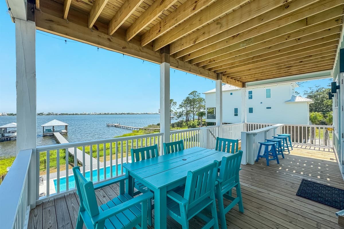 This expansive covered deck features a large outdoor dining table, offering stunning water views and an overlook of the private pool and dock.