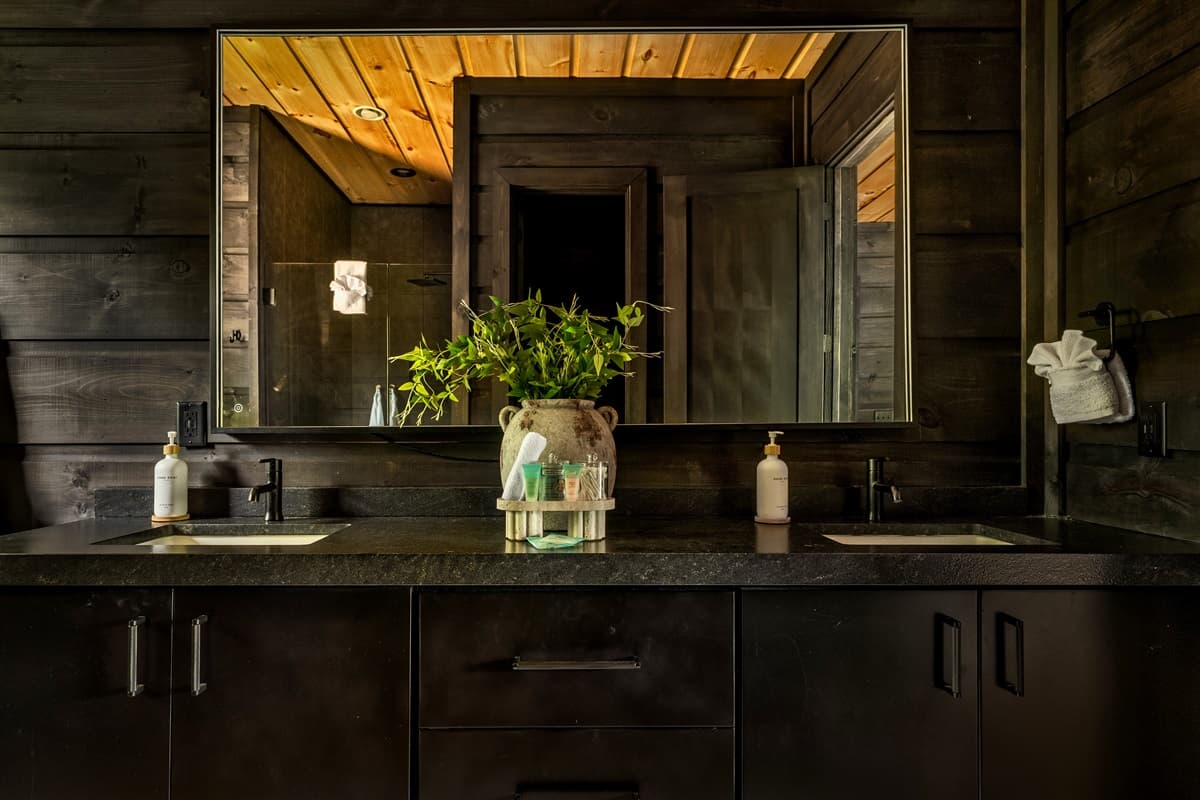 This stylish bathroom features a modern double vanity with sleek black sinks and ample mirror space, set against elegant dark wooden walls.