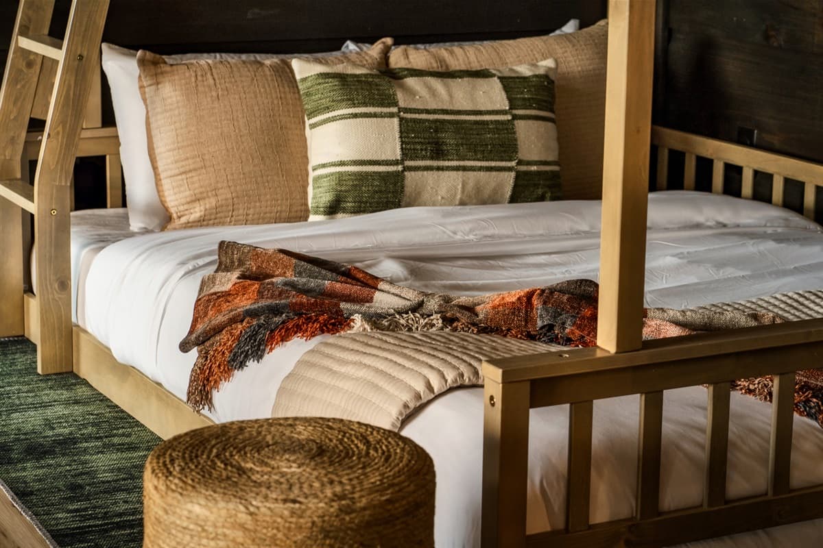 This comfortable bunk bed features soft bedding, a mix of decorative pillows, and a warm plaid throw, creating a cozy sleeping space.