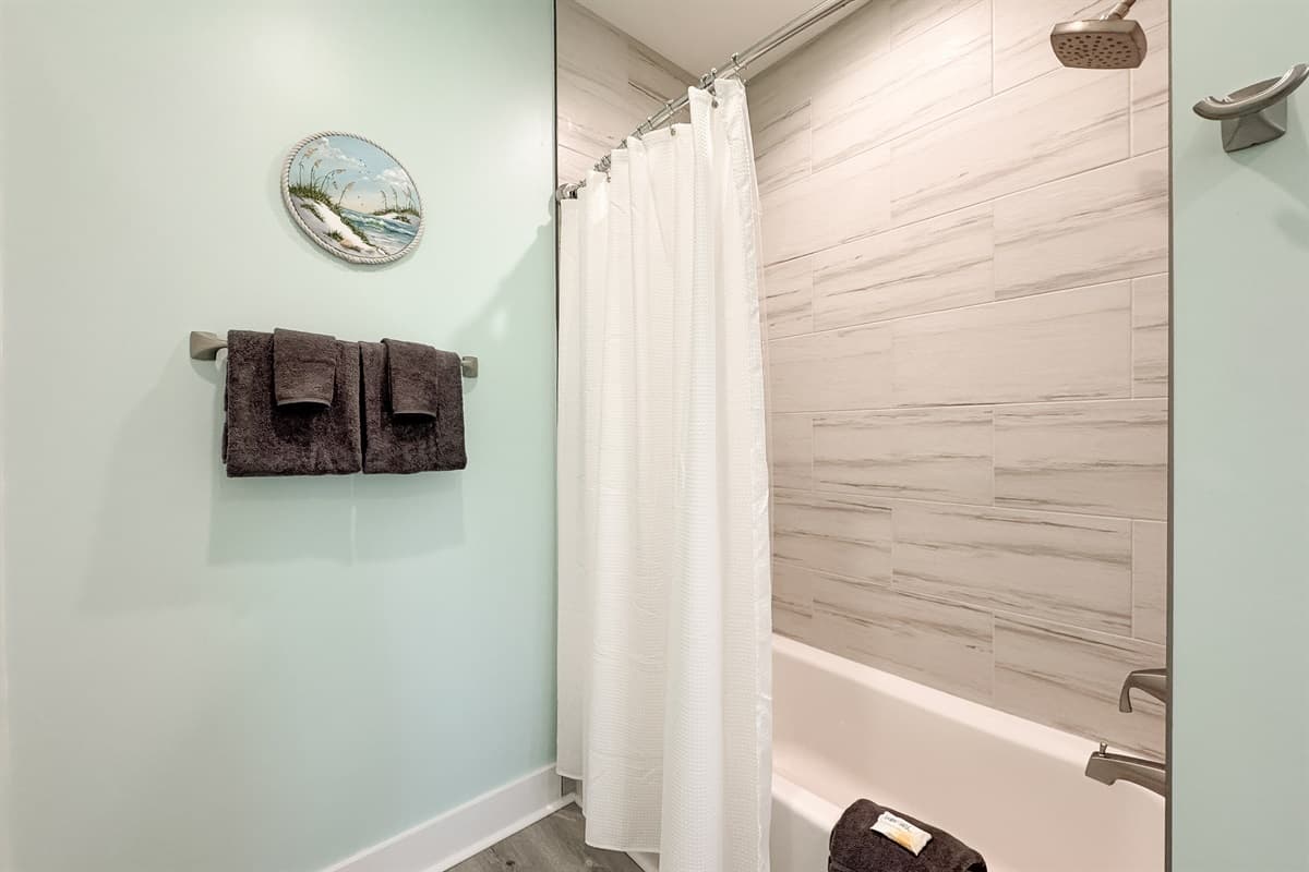 This bright bathroom features a combination bathtub and shower with elegant tiled walls and a refreshing coastal aesthetic.