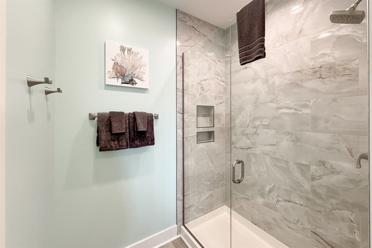 Enjoy a refreshing experience in the large walk-in shower, complete with beautiful light-colored marble-look tile work and a convenient built-in niche for toiletries. The clear glass door adds to the contemporary and open feel of the space.