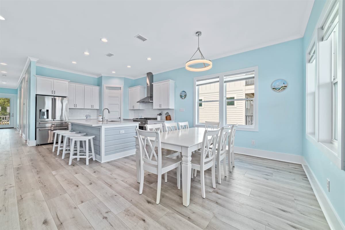 This bright and inviting kitchen features contemporary white shaker cabinets and a large island with comfortable bar stools. Its open design flows seamlessly into the dining area, creating an ideal space for preparing meals and enjoying time with loved one