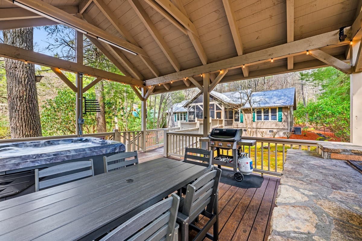 Wide View of the Covered Deck with Dining Table, Hot Tub, String Lights, Hot Tub Towel Holder and Cabin Backdrop