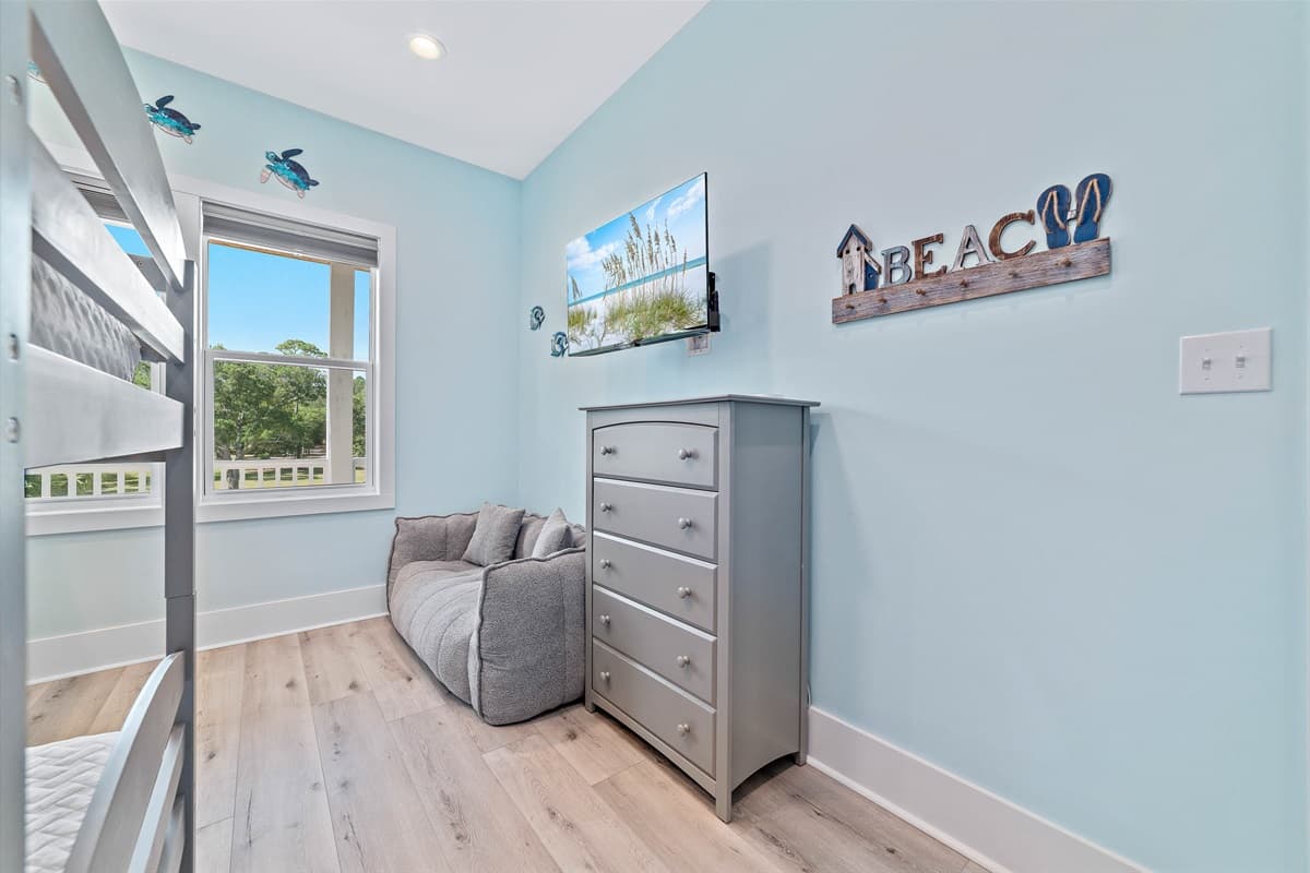 deal for additional guests or a relaxed lounging space, this inviting bedroom includes a plush sofa and a convenient wall-mounted television. The light blue walls and charming "BEACH" sign create a delightful coastal ambiance.