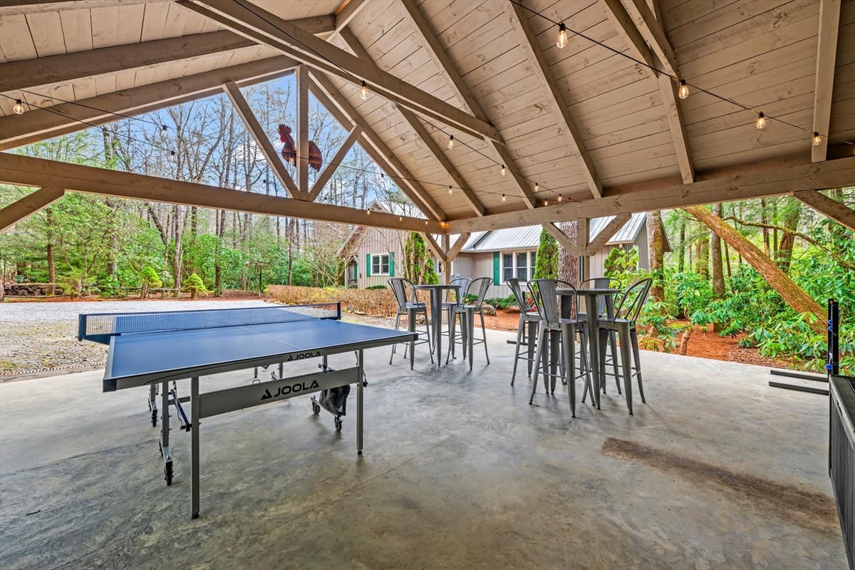 Wide-Angle View of the Covered Carport Game Area with Ping Pong, Outdoor Jenga, String Lights and Forest Views