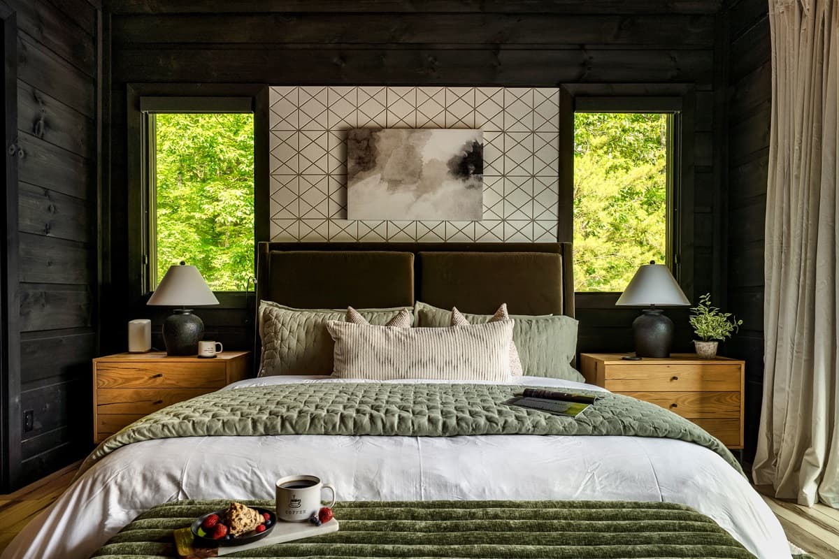 Drift off to sleep in this serene primary bedroom, featuring a large bed with a plush olive-green headboard and soft bedding, flanked by matching wooden nightstands with elegant lamps. The modern accent wall and natural light create a peaceful and sophisti