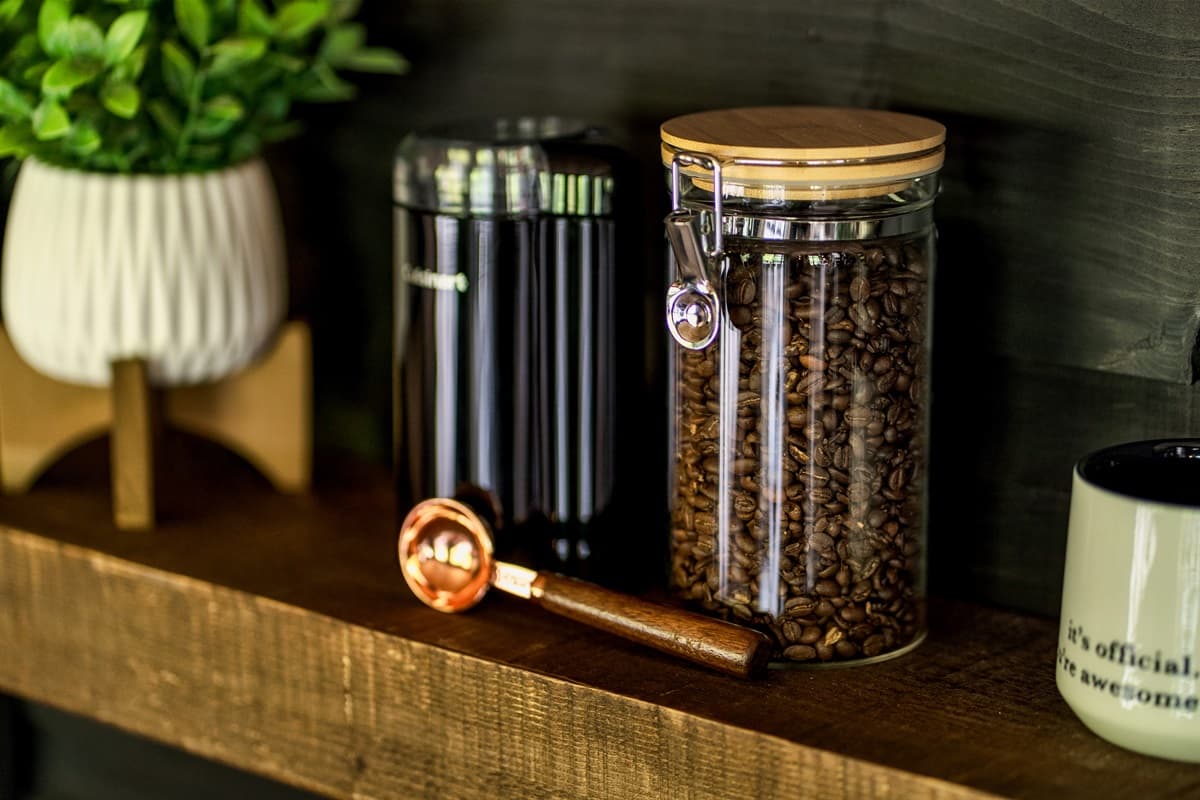 A perfectly organized coffee station features fresh beans in a glass jar, a modern coffee canister, and a stylish copper scoop, ready for your morning brew.