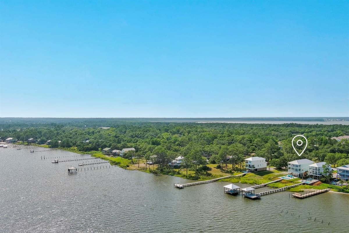 This stunning aerial view showcases a peaceful coastal community with waterfront homes, private docks, and an abundance of lush green trees.