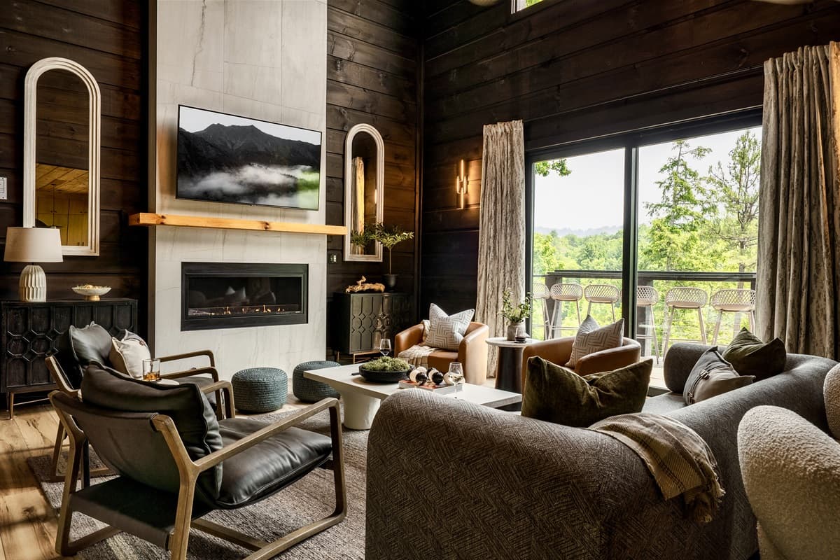 This sophisticated living room features a cozy fireplace, comfortable seating, and large windows offering panoramic views of the natural landscape.