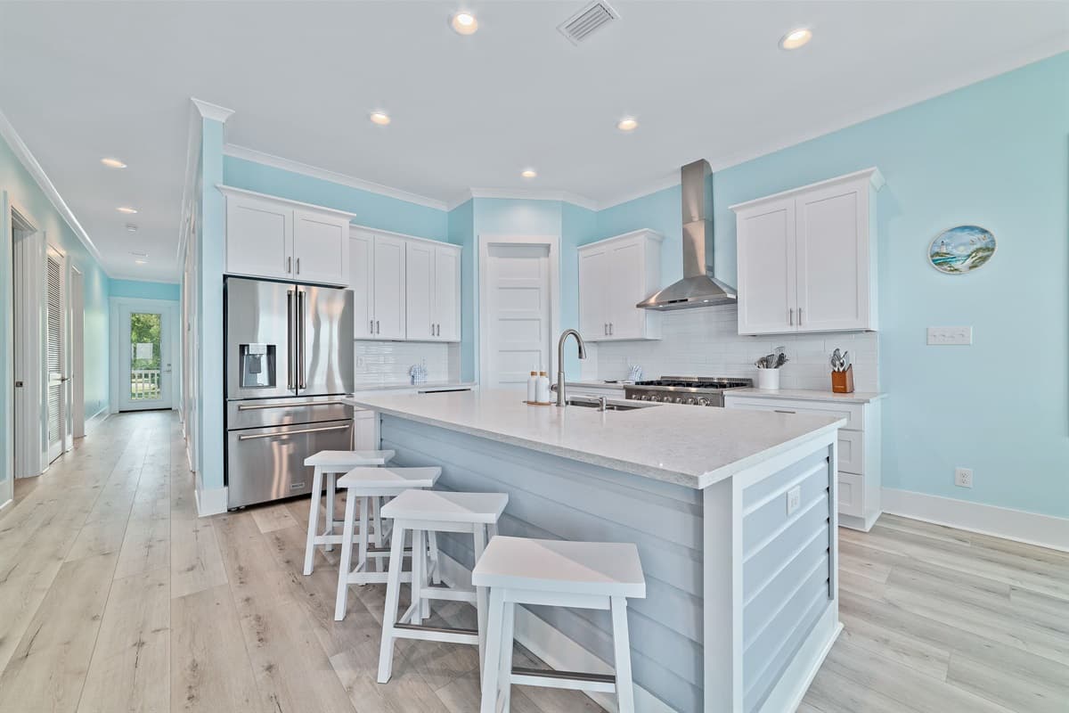The bright and modern kitchen features white cabinetry, ample counter space, and an island with bar seating, all flowing into an inviting hallway.