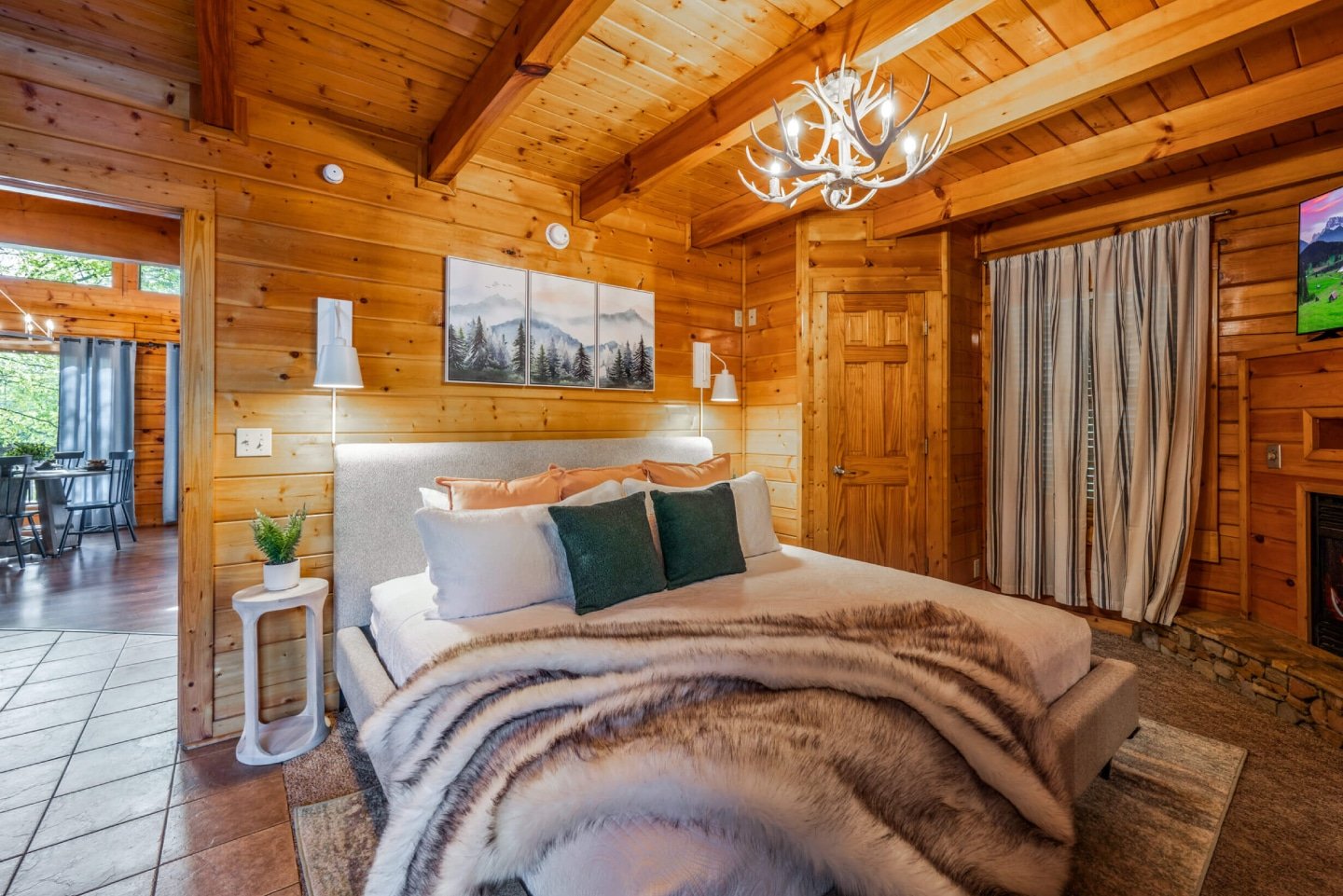 This charming log cabin bedroom provides a luxurious and comfortable sanctuary, boasting a plush king bed, a cozy fireplace, and an open layout that flows seamlessly into additional living space.